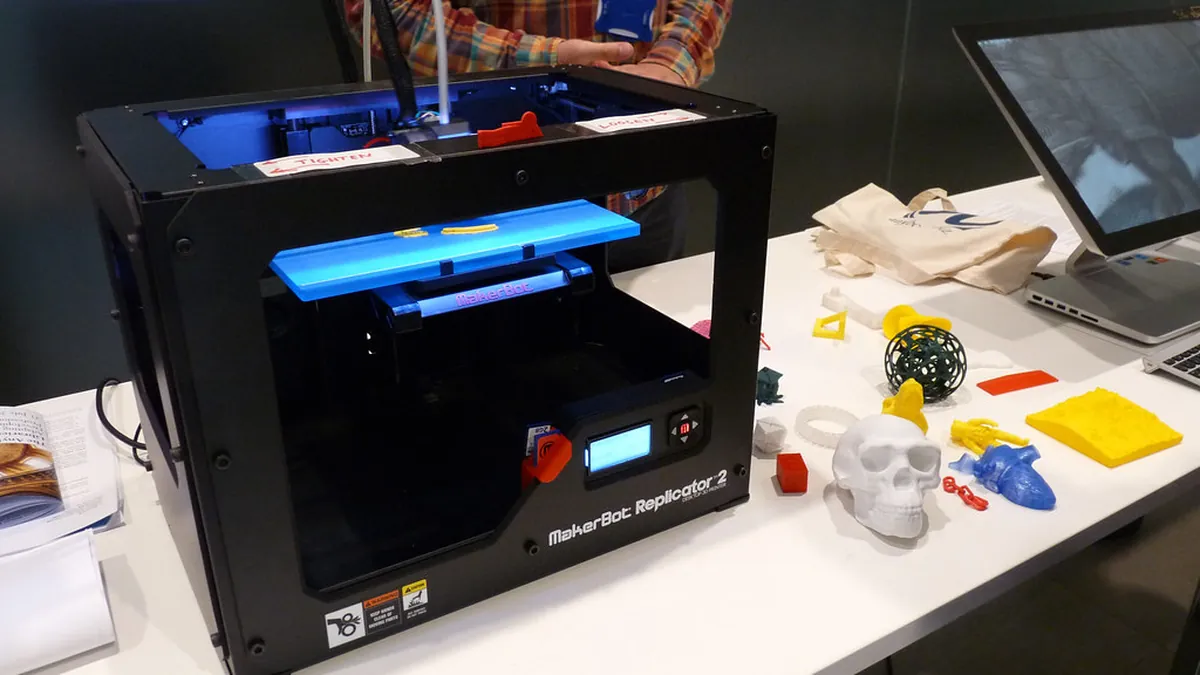 A desktop 3D printer mid-print, with several finished parts beside it.