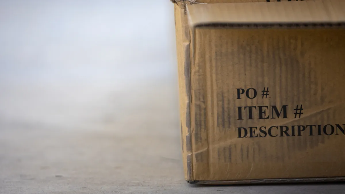 Esquina de una caja de cartón abierta sobre el suelo, con las casillas de pedido y descripción impresas en un lado.
