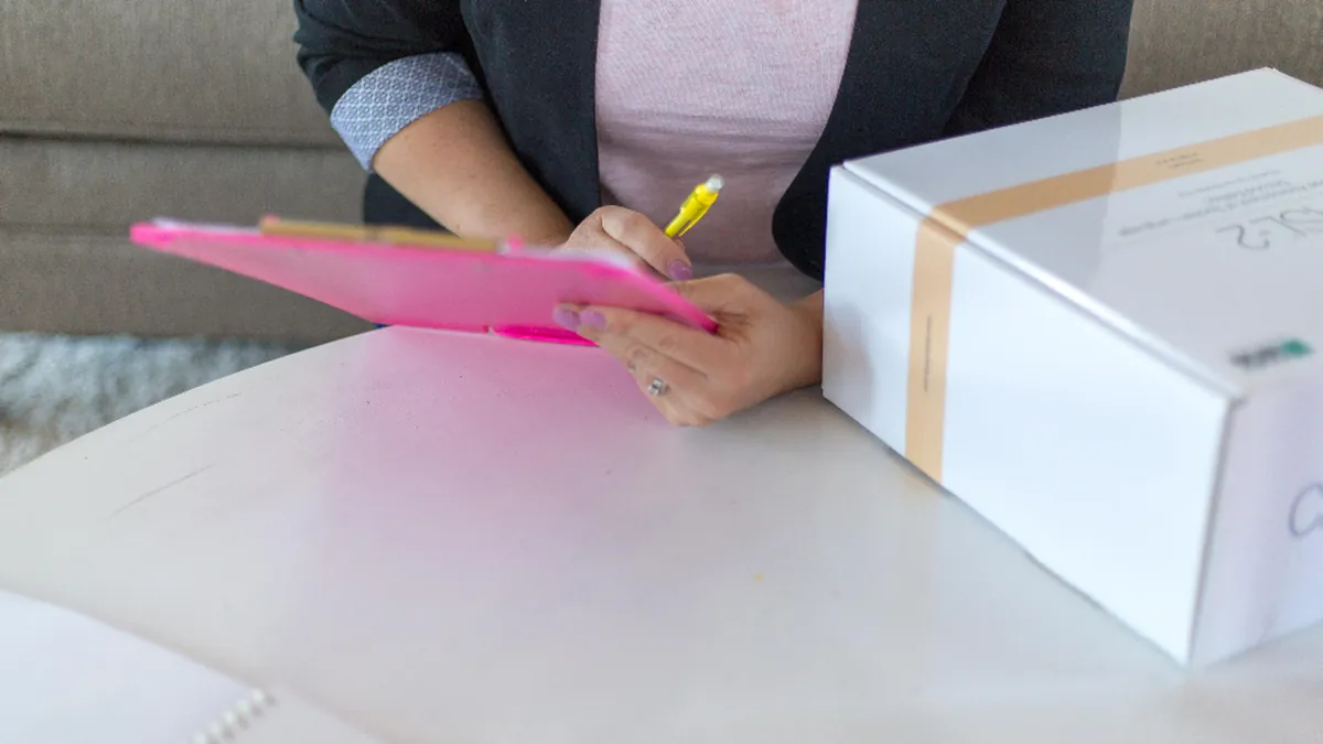 Persona anotando en una tablilla junto a una caja preparada para enviar.
