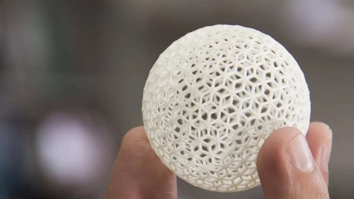 A hand holding a 3D printed lattice sphere in white plastic.