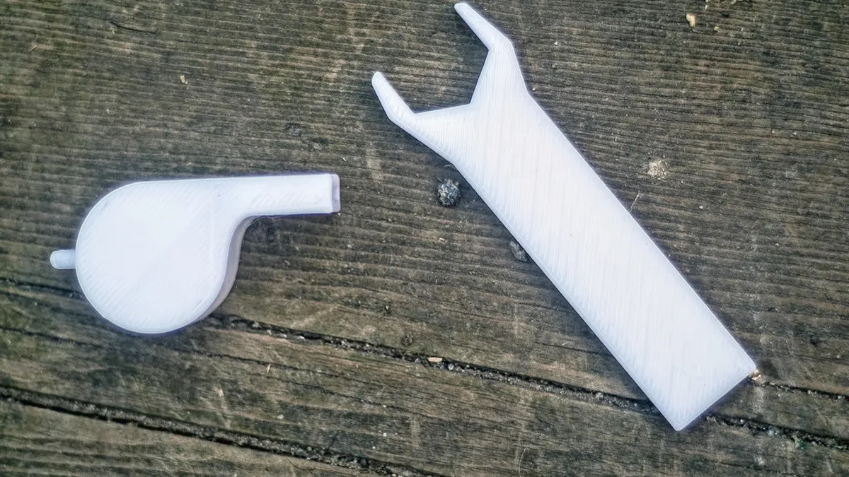 Dos piezas blancas recién impresas en 3D sobre unos tablones de madera, con las líneas de capa a la vista.